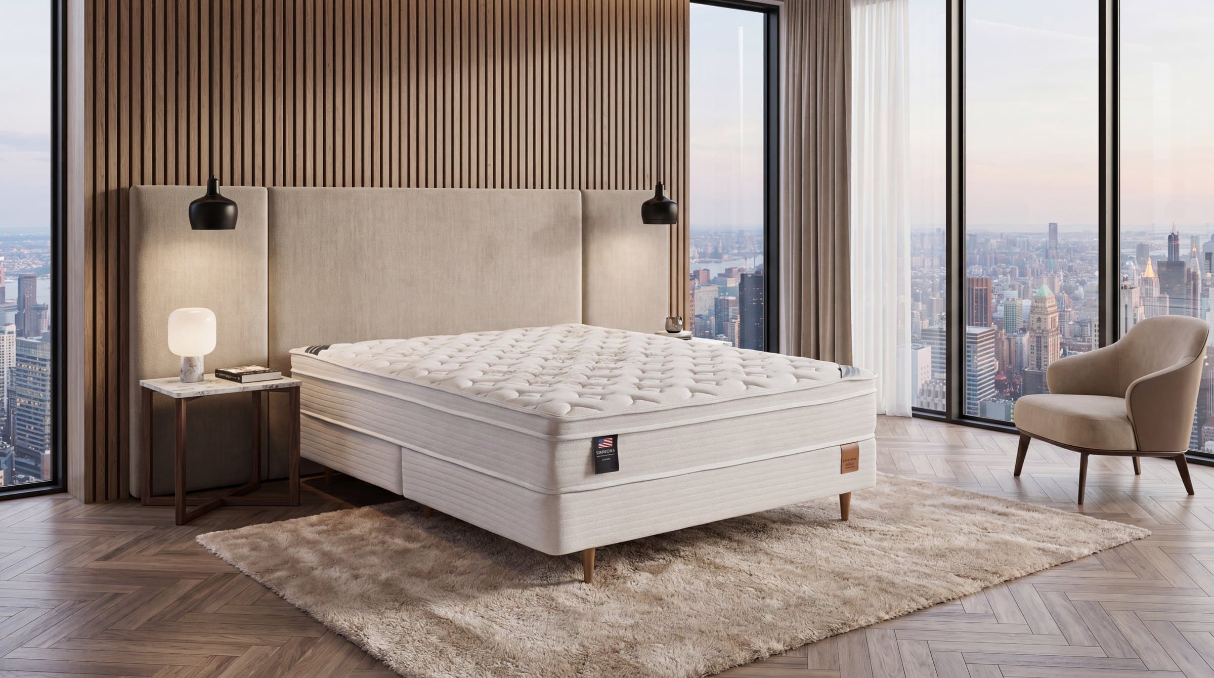 Cama com cabeceira estofada bege e ripado, luminárias pendentes e vista da cidade ao entardecer
