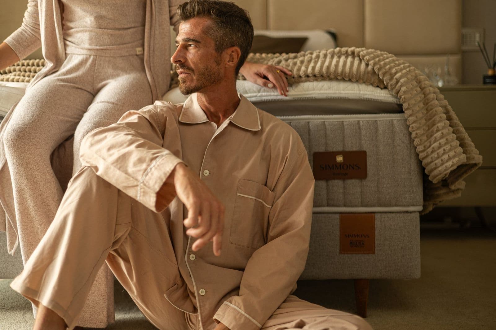 Homem de pijama sentado no chão ao lado da cama Simmons