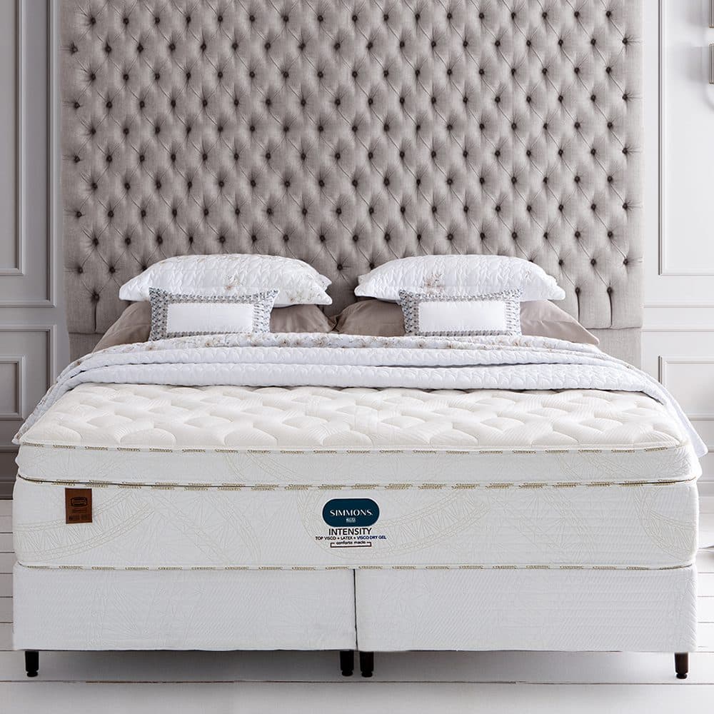 Conjunto Simmons Intensity Plush montado diante de uma cabeceira capitonê clara, com o pillow top alto em destaque